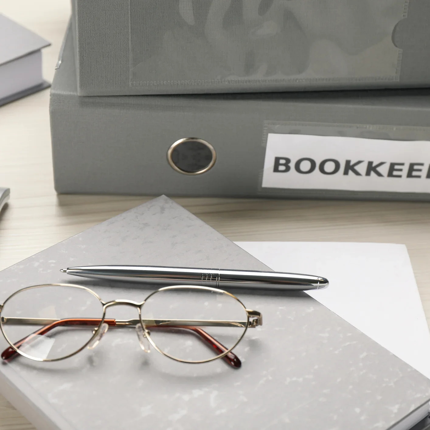 Desk with a book, pen, and glasses on top of it, as well as a calculator
